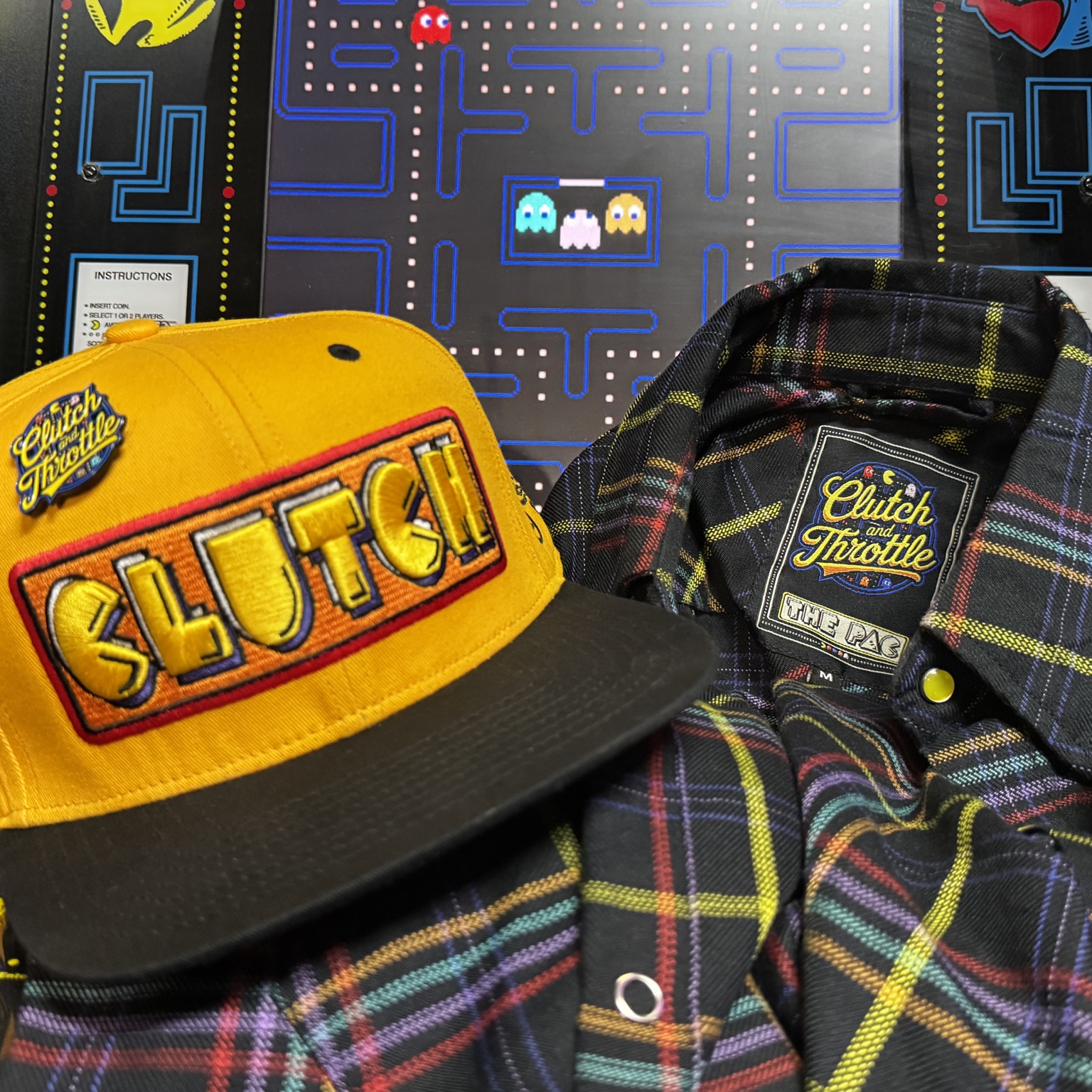 Clutch & Throttle The Pac flannel and yellow Clutch hat in front of an arcade cabinet